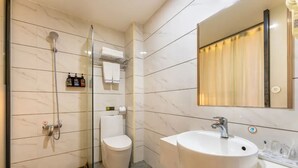 A modern bathroom with a glass-enclosed shower, a toilet, and a sink with a mirror above. - Ruijing Hotel (Dongguan)