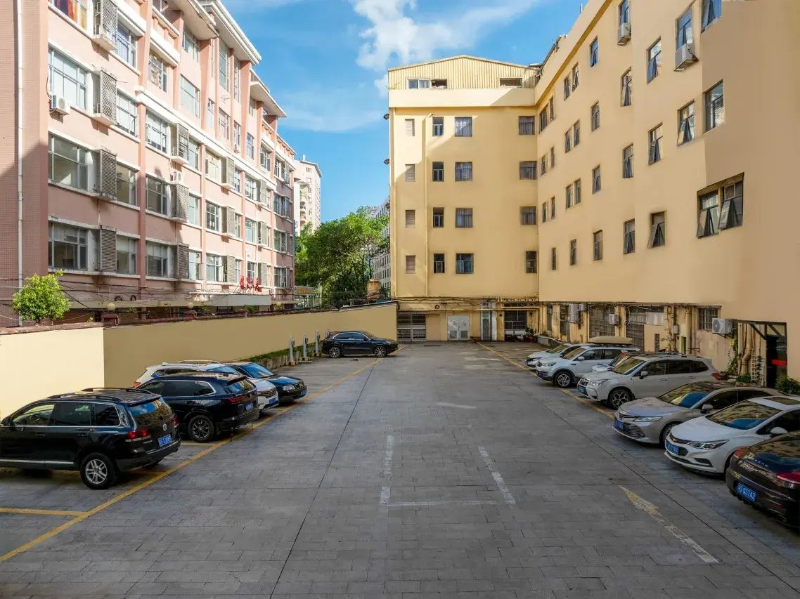 Un estacionamiento con varios coches aparcados en filas, junto a un edificio de varios pisos y balcones.