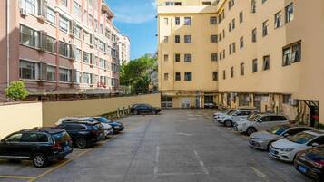 Un estacionamiento con varios coches aparcados en filas, junto a un edificio de varios pisos y balcones.