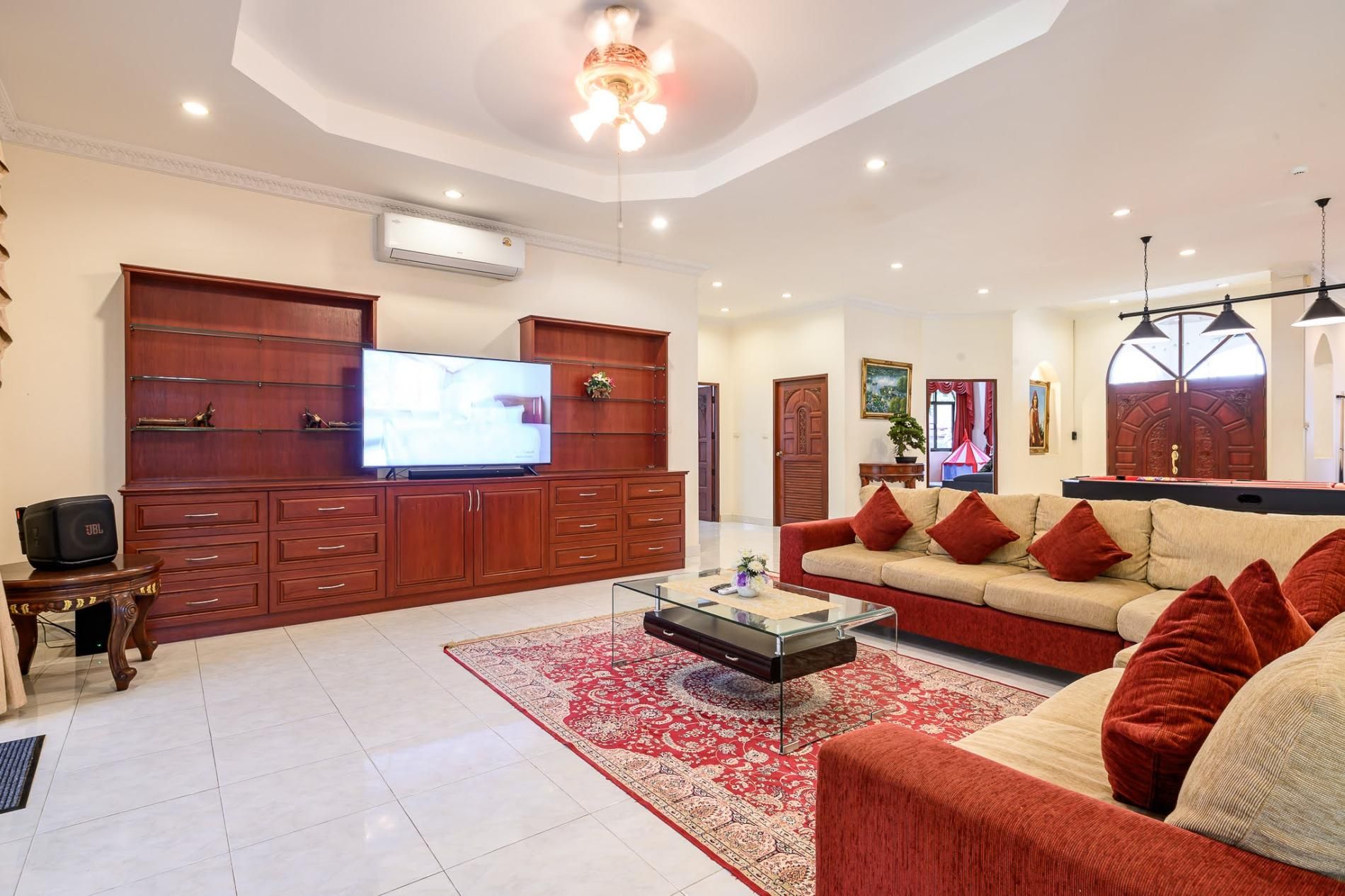 A spacious living room with a large flat-screen TV, a sofa set, a coffee table, and a red patterned rug.