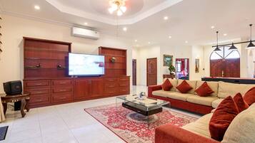 A spacious living room with a large flat-screen TV, a sofa set, a coffee table, and a red patterned rug.