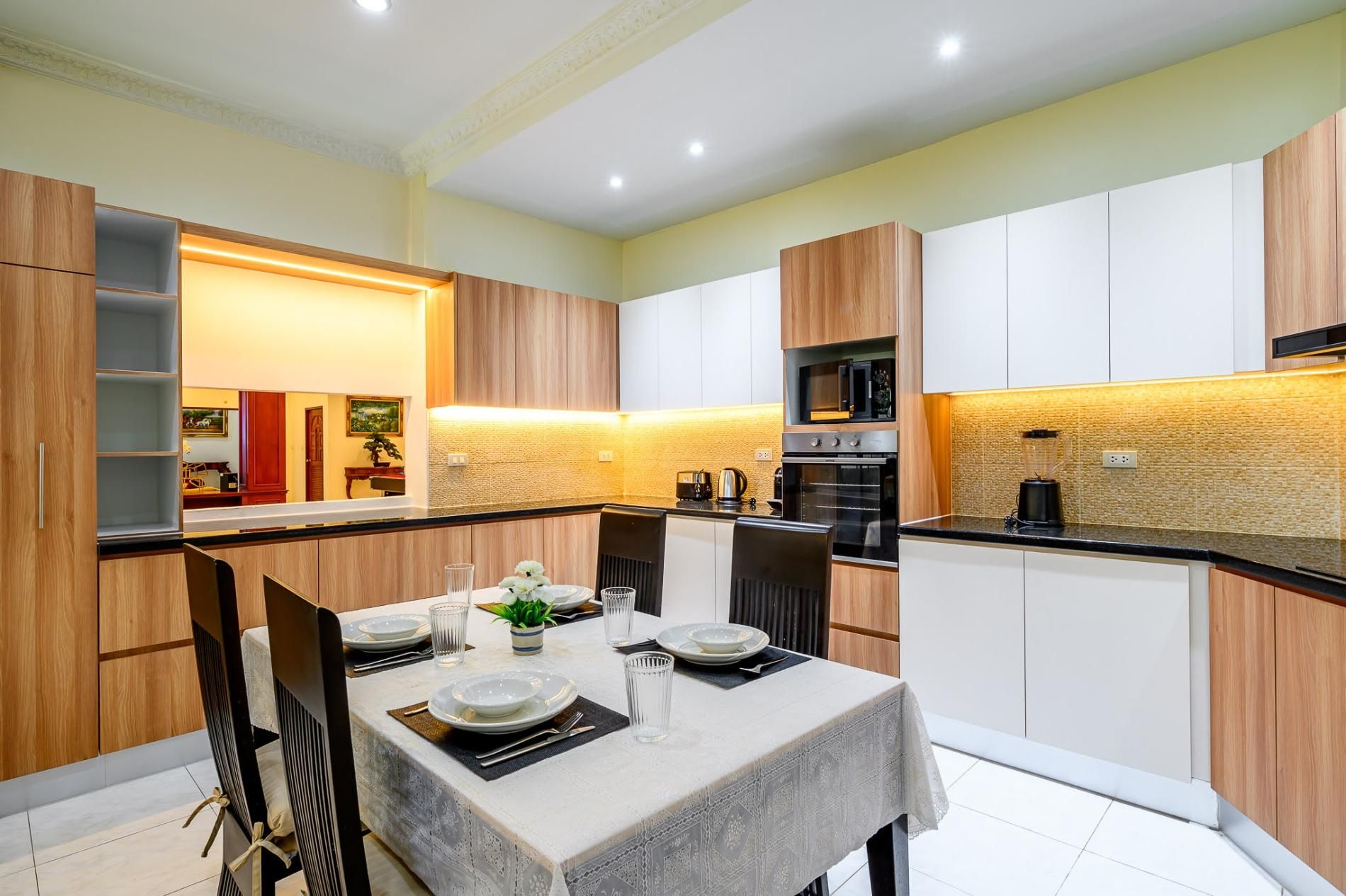 A modern kitchen with a dining area, featuring a table set for four, a microwave, and a coffee maker.