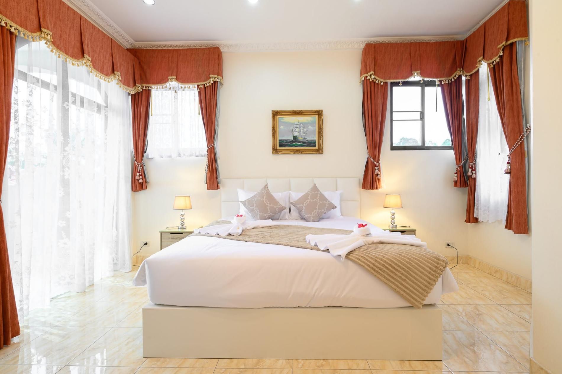 A hotel room with a large bed, two bedside tables, a painting on the wall, and red curtains.