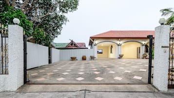 A gated entrance with a tiled driveway leading to a building with a red roof and a covered area with columns.