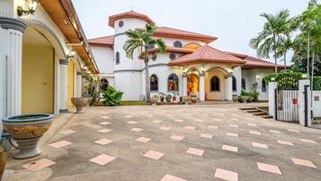 A spacious courtyard with a tiled floor, a white building with red-tiled roof, and palm trees.