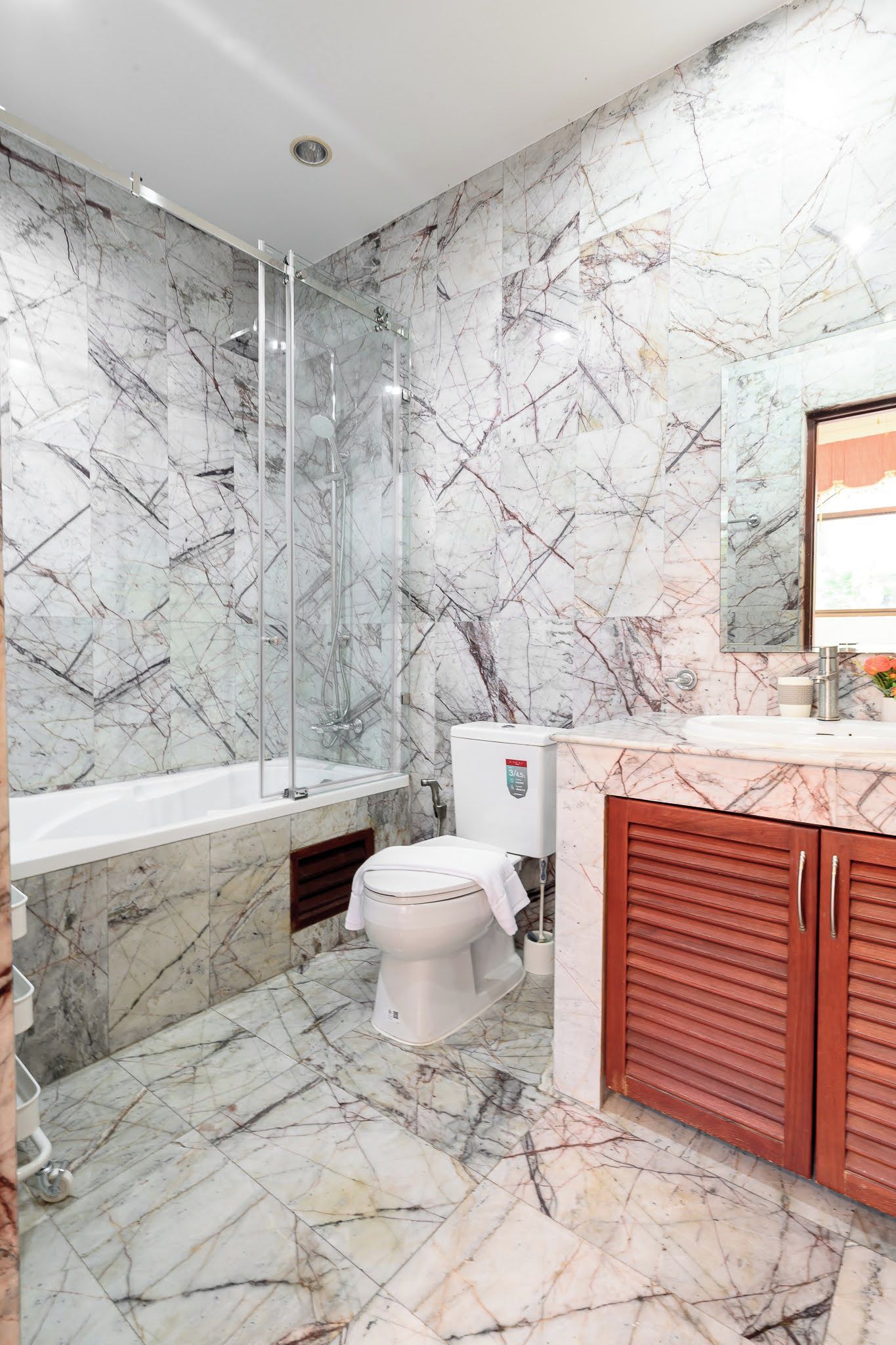 A bathroom with a glass shower enclosure, a toilet, and a sink with a marble countertop.