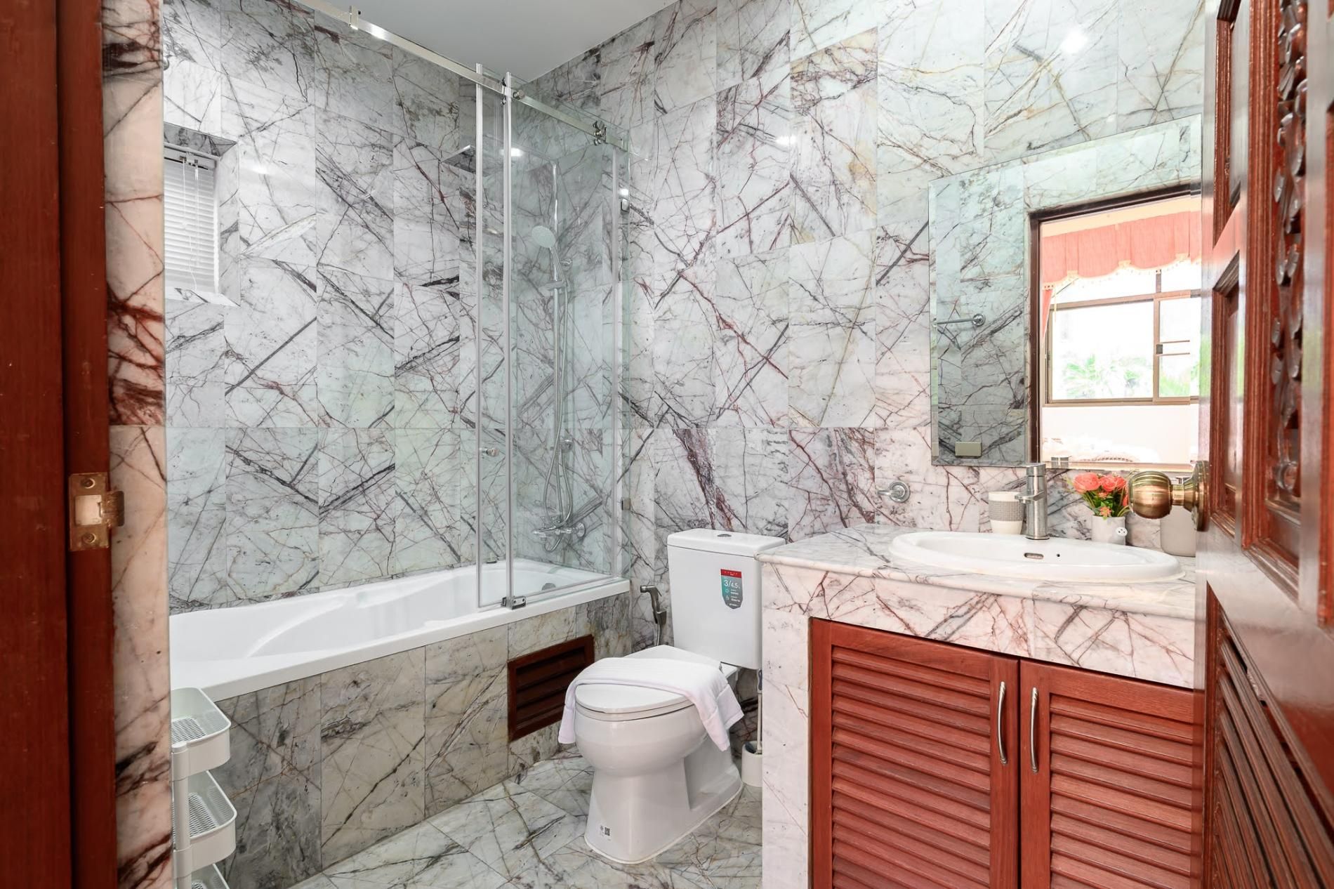 A bathroom with a marble wall, a bathtub, a toilet, and a vanity with a mirror.