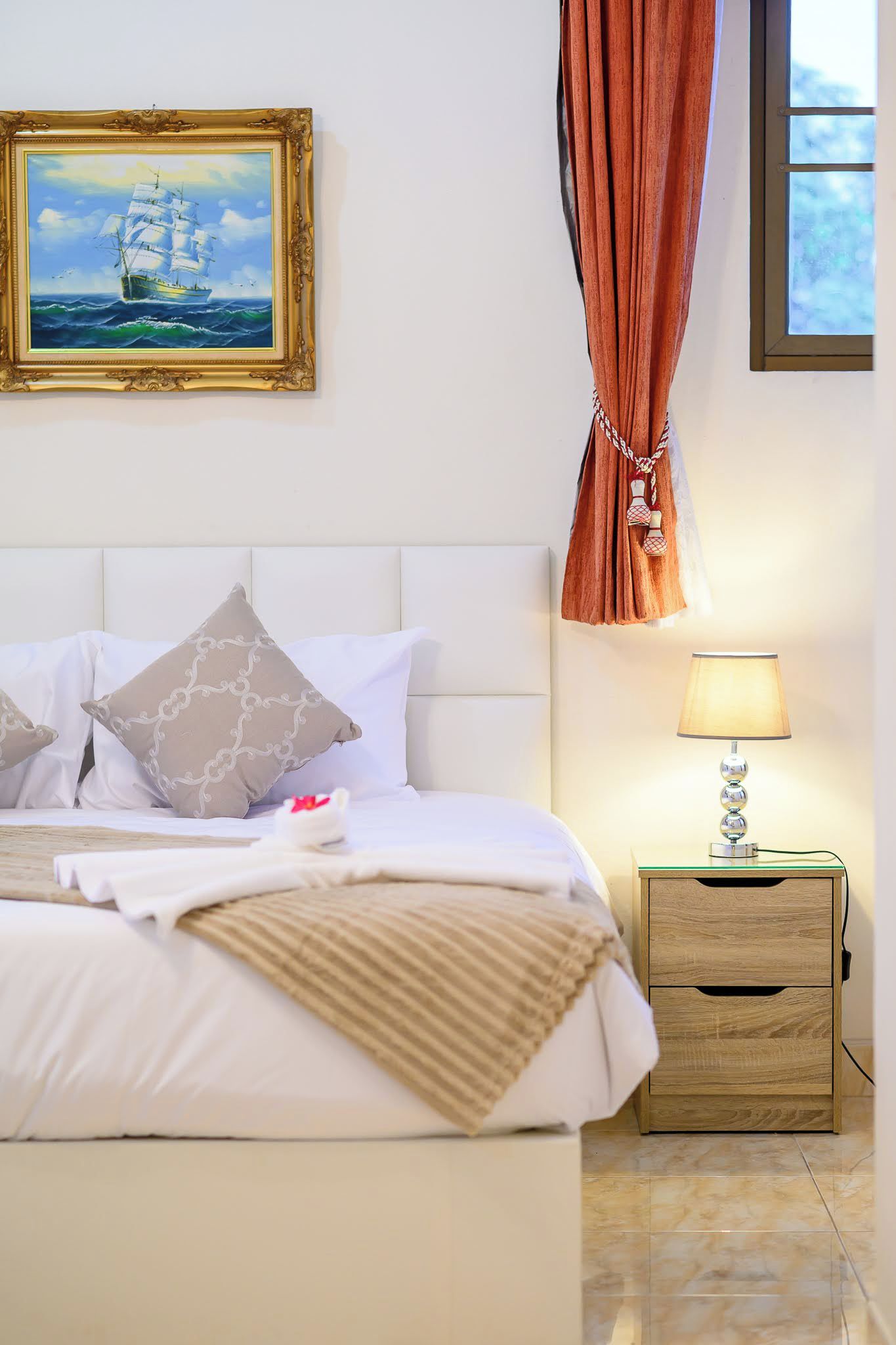 Una cama bien hecha con almohadas, una lámpara de noche y una mesita de noche de madera con cajones.