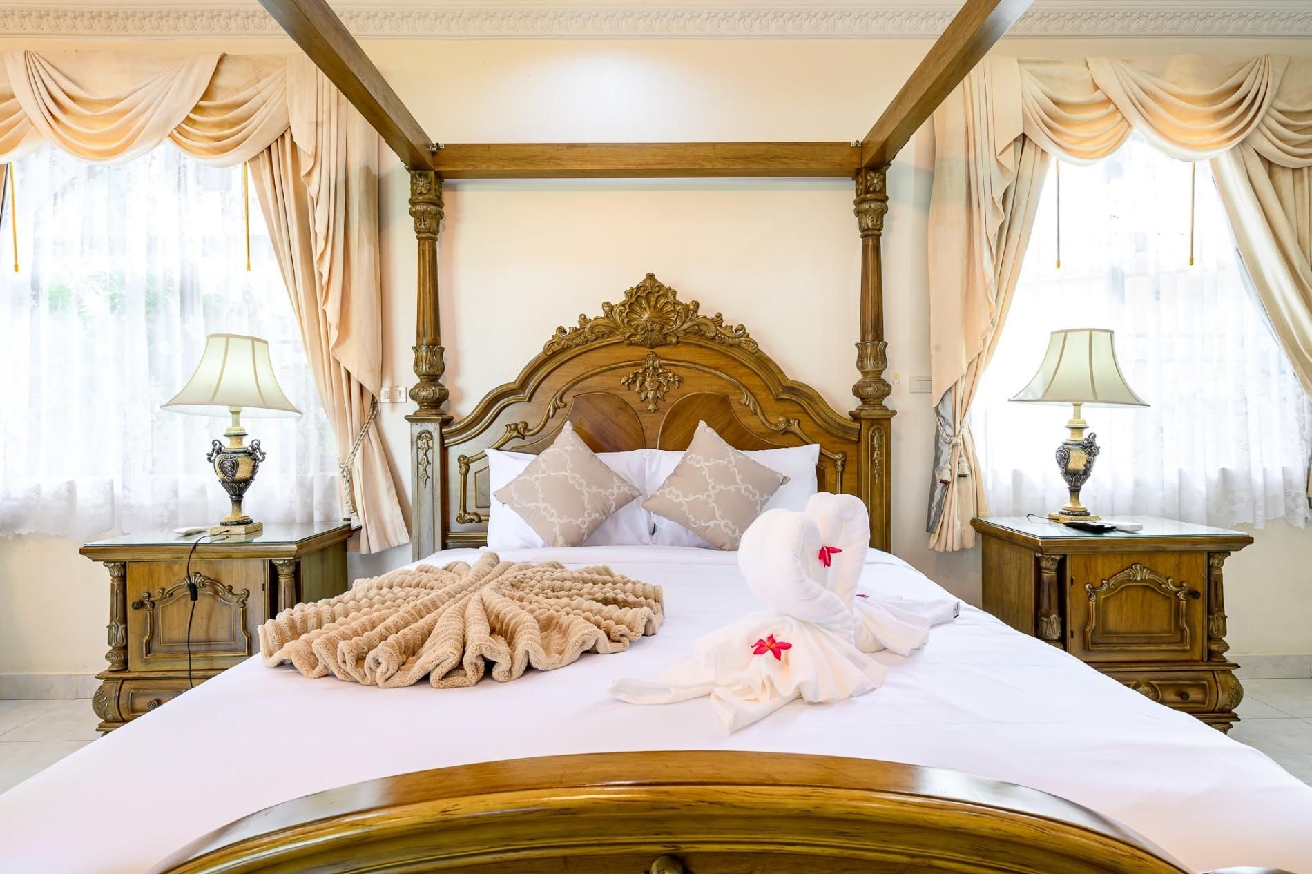 A hotel room with a large bed, ornate headboard, two bedside tables with lamps, and curtains.