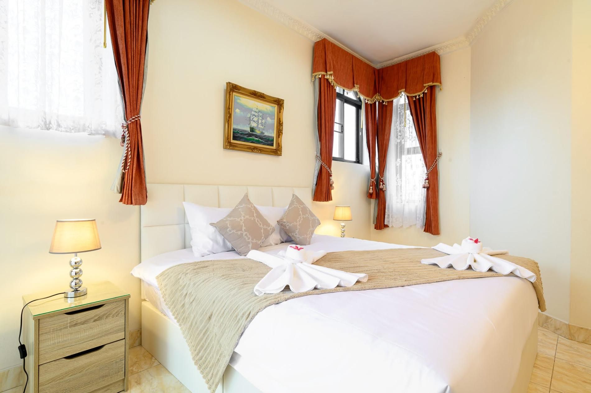 A hotel room with a bed, two bedside tables, a painting on the wall, and curtains.