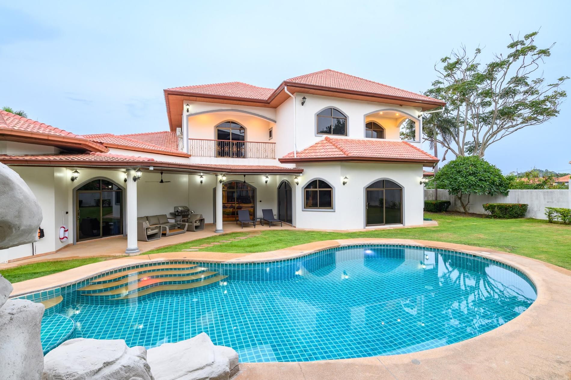 A two-story house with a swimming pool, outdoor seating, and a covered patio.