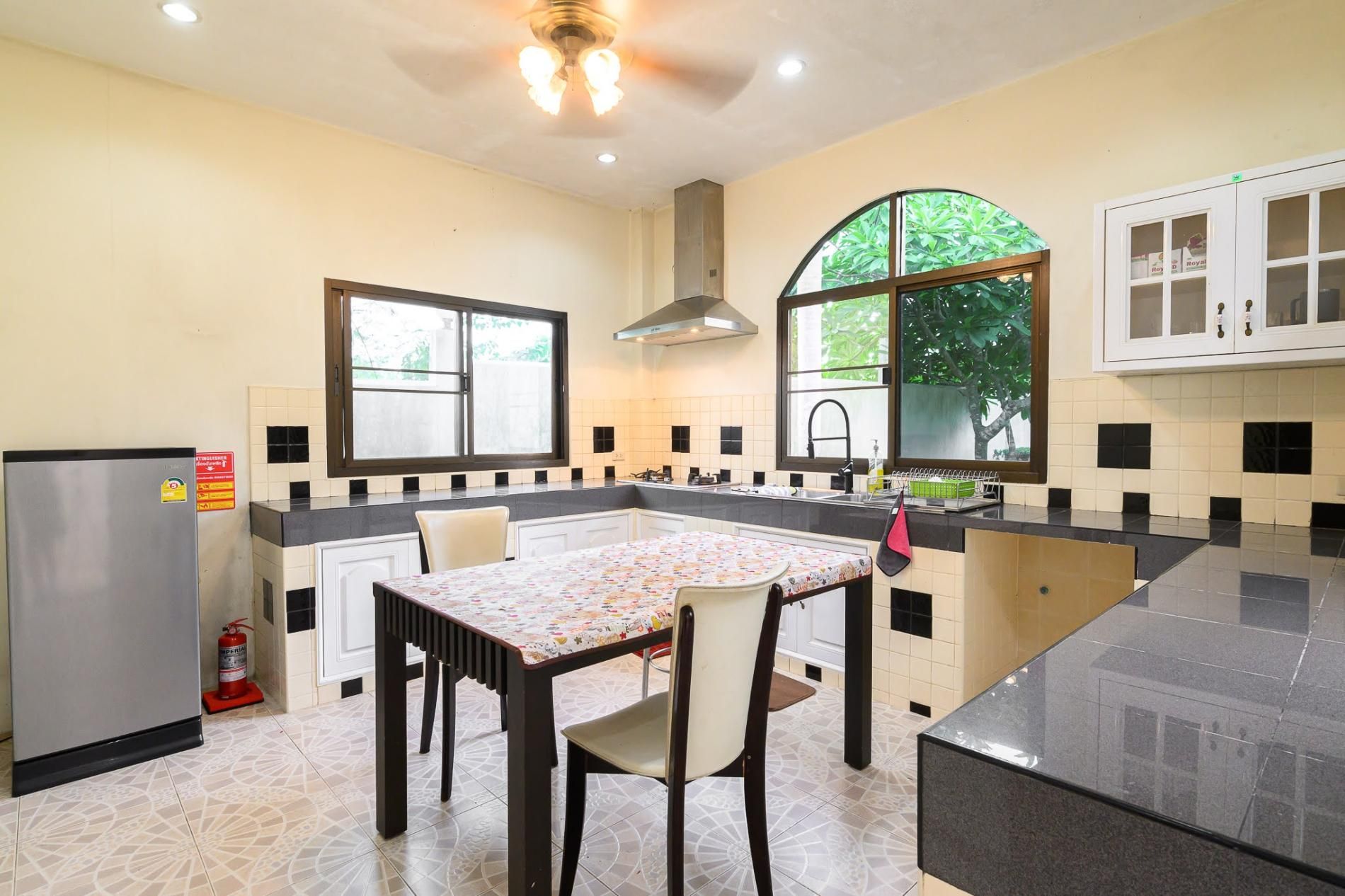 A kitchen with a dining table, chairs, a refrigerator, and a window with a view of greenery.