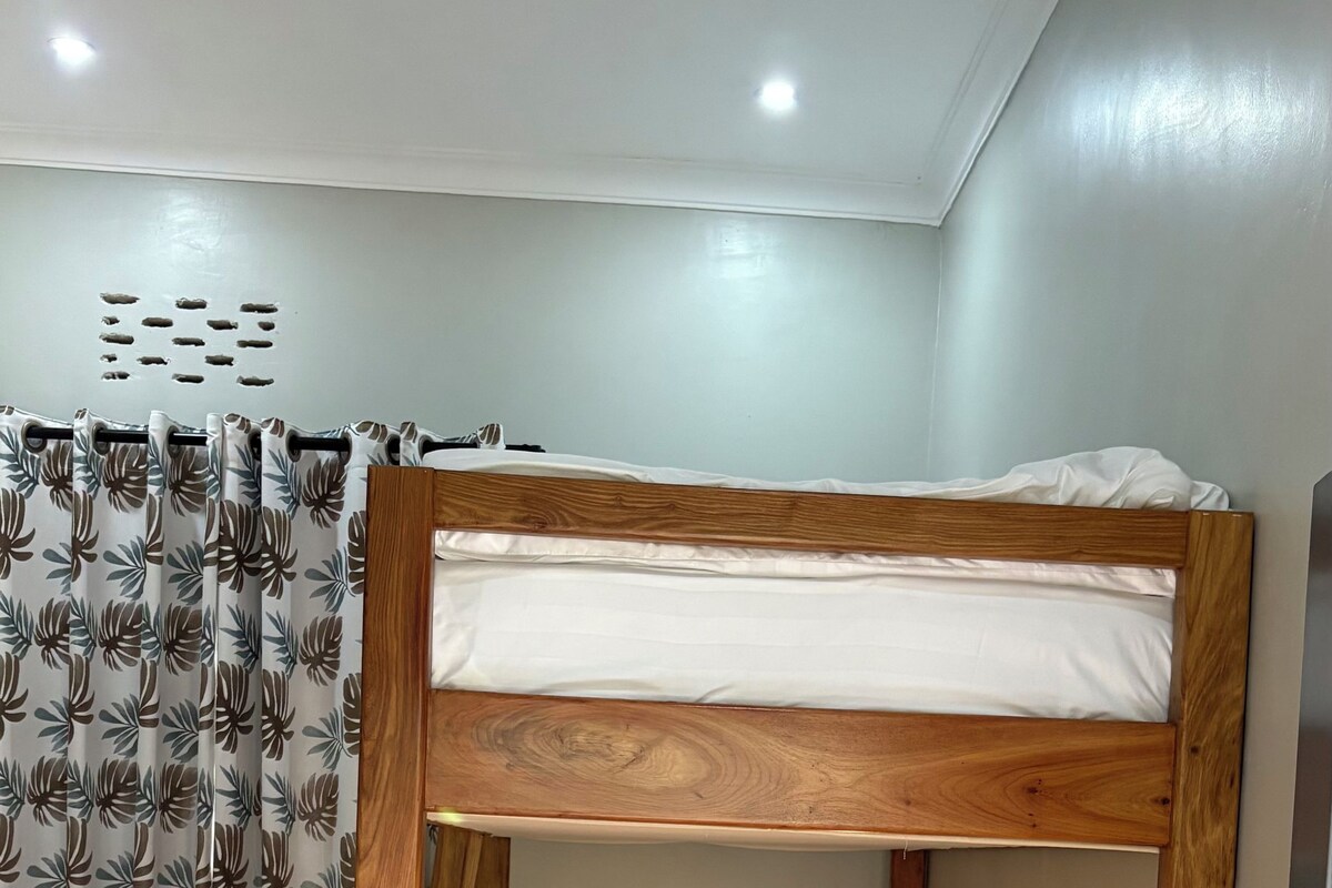 Una cama litera con escritorio y silla, una lámpara pequeña y una ventana con cortina.