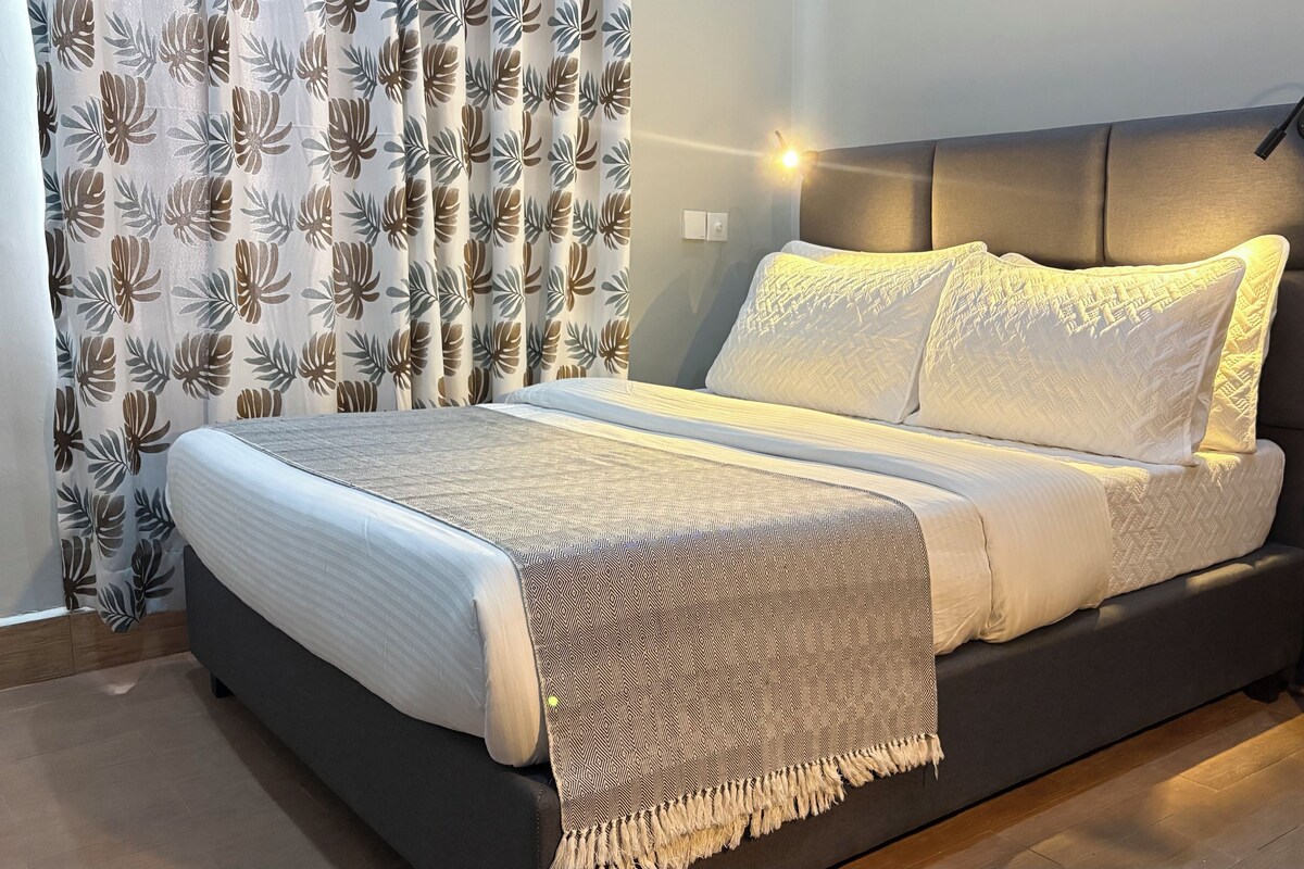 Un dormitorio moderno con cama, cortinas y una lámpara de noche.