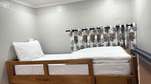 A single bed with a wooden frame, white bedding, and a pillow. - Siku Lodge (Arusha)