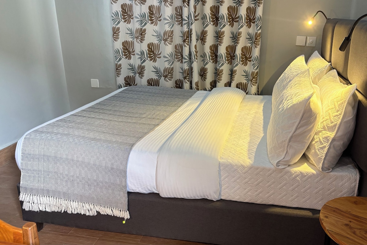 A bed with a patterned bedspread, a headboard with integrated lighting, and a bedside table with a round wooden top.