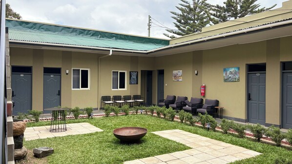 A building with numbered doors, outdoor seating, a fire extinguisher, and a small garden area. - Siku Lodge (Arusha)