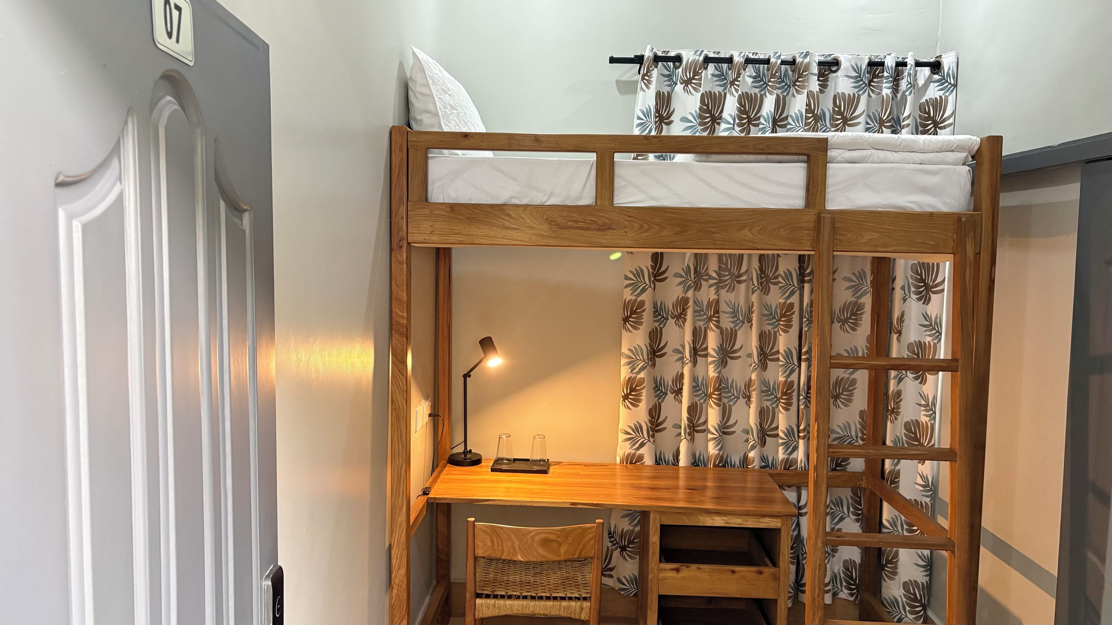 A bunk bed with a desk and chair, a lamp, and a curtain with a leaf pattern.