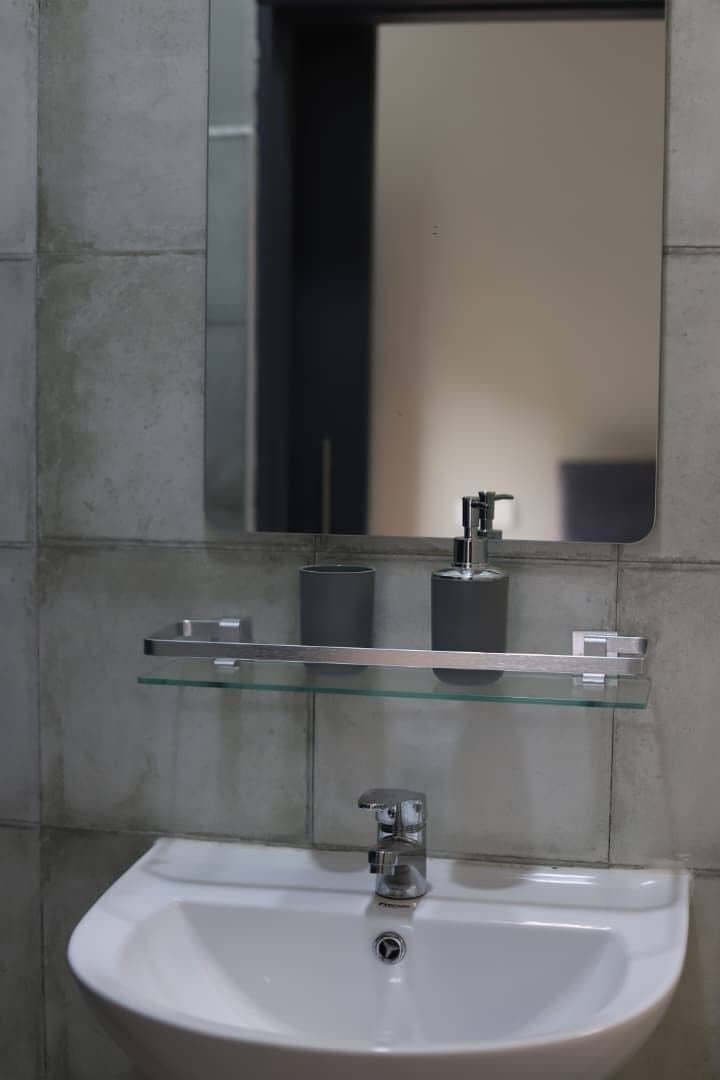 A bathroom with a white sink, a glass shelf with toiletries, and a mirror above.