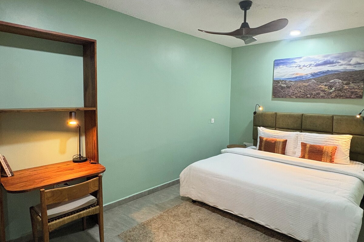 A bedroom with a bed, a desk, a chair, a ceiling fan, and a wall-mounted picture.