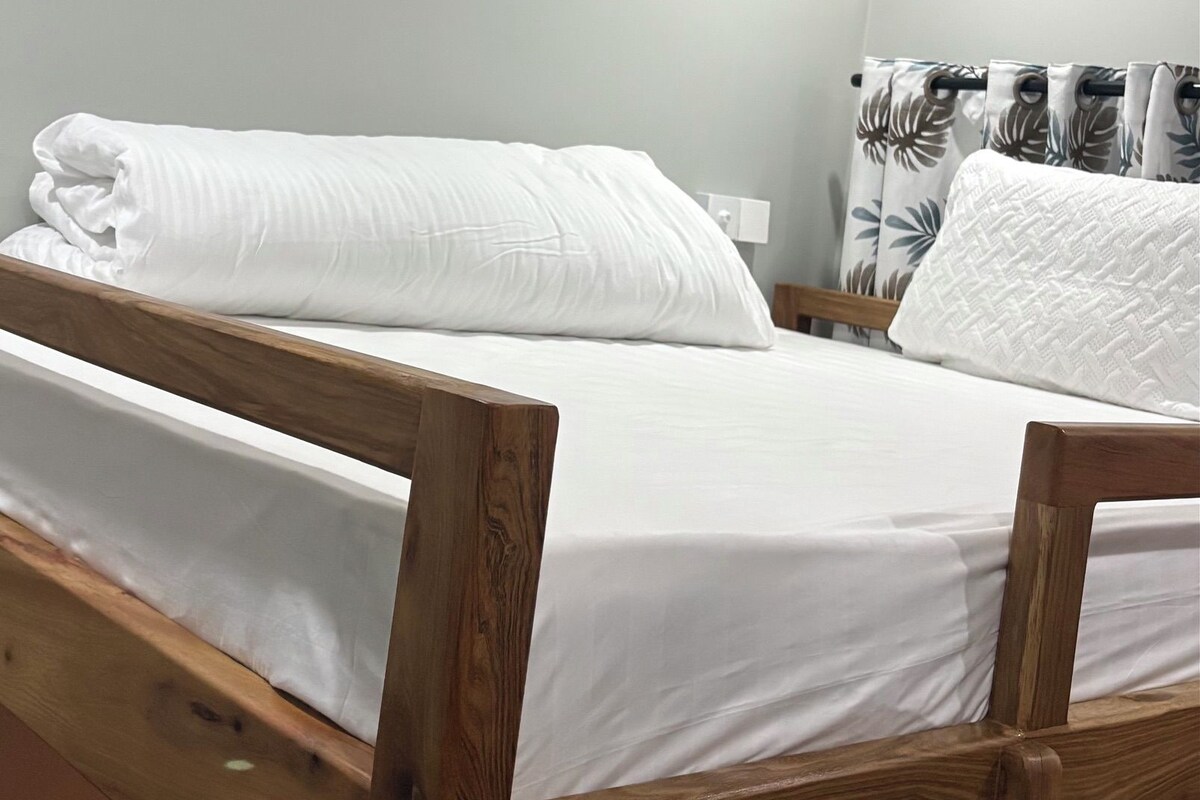 Una cama individual con ropa blanca en una habitación de paredes claras y cabecera de madera.