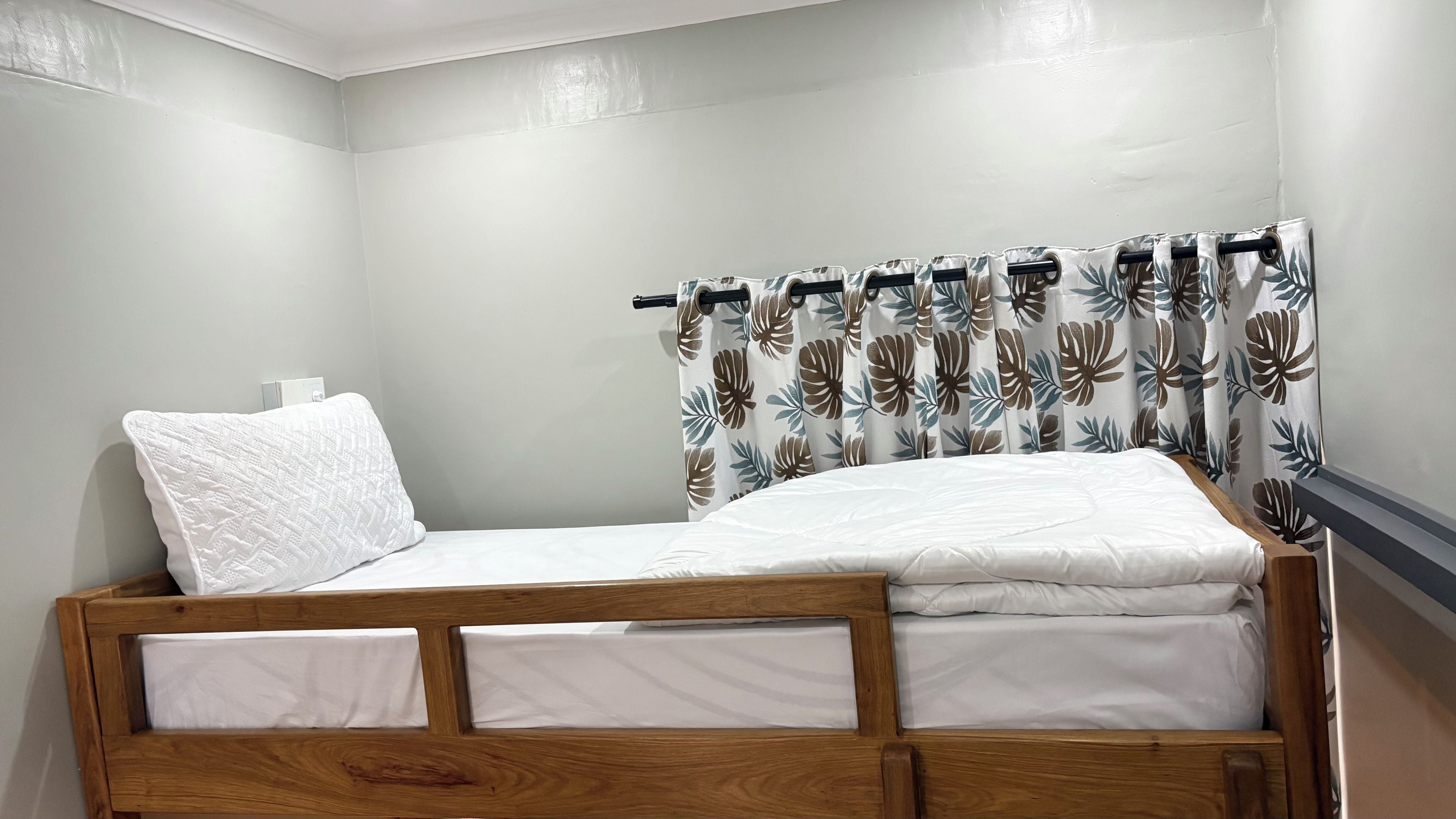 A single bed with a wooden frame, white bedding, and a pillow.
