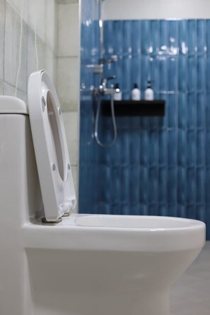 Un baño moderno con inodoro blanco, cortina de ducha azul y cabezal de ducha visible.