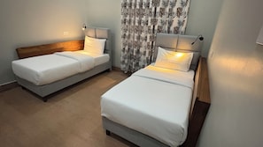 Two single beds with headboards, a wooden headboard bed, and a curtain with a leaf pattern. - Siku Lodge (Arusha)