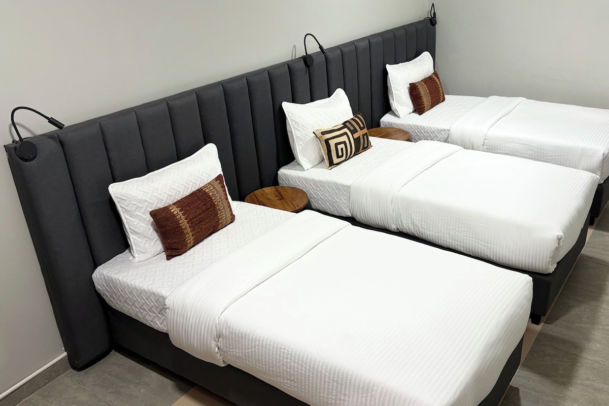 Una habitación de hotel con tres camas individuales, cada una con ropa blanca y almohadas decorativas.