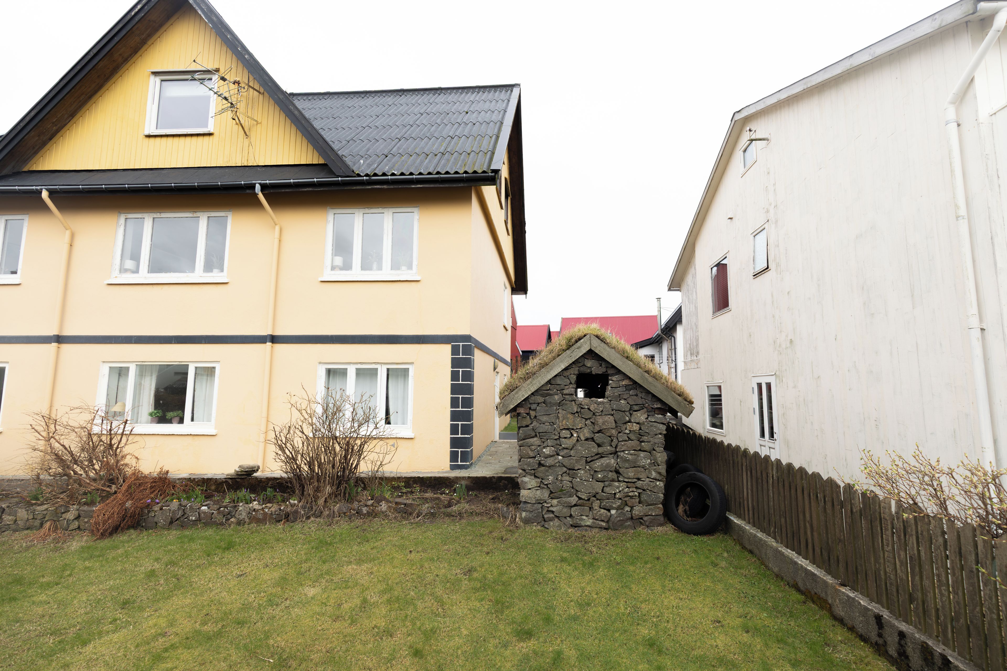 A two-story house with a stone extension, a fenced yard, and a neighboring building.