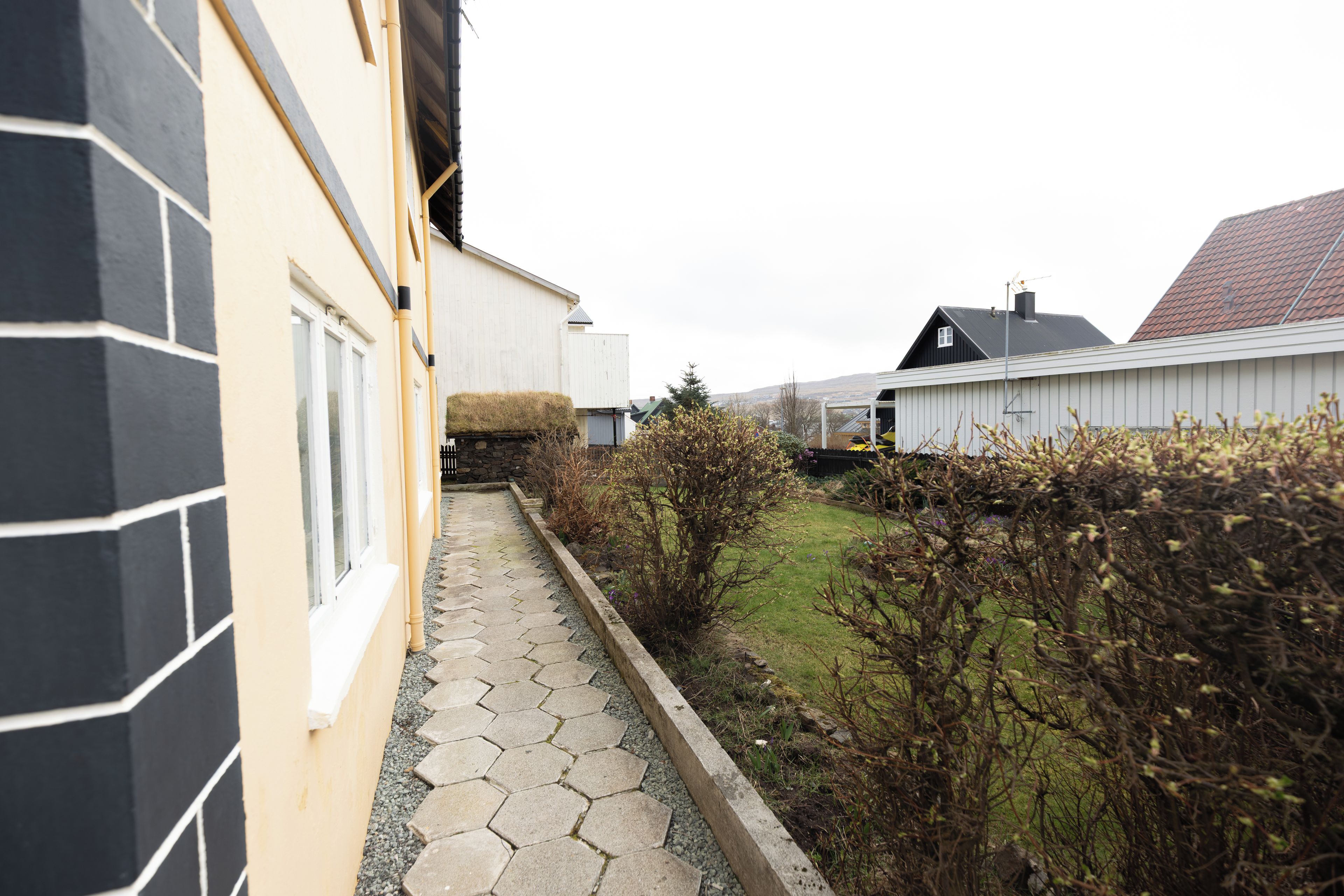 A residential property with a paved pathway, a stone wall, and a grassy yard.