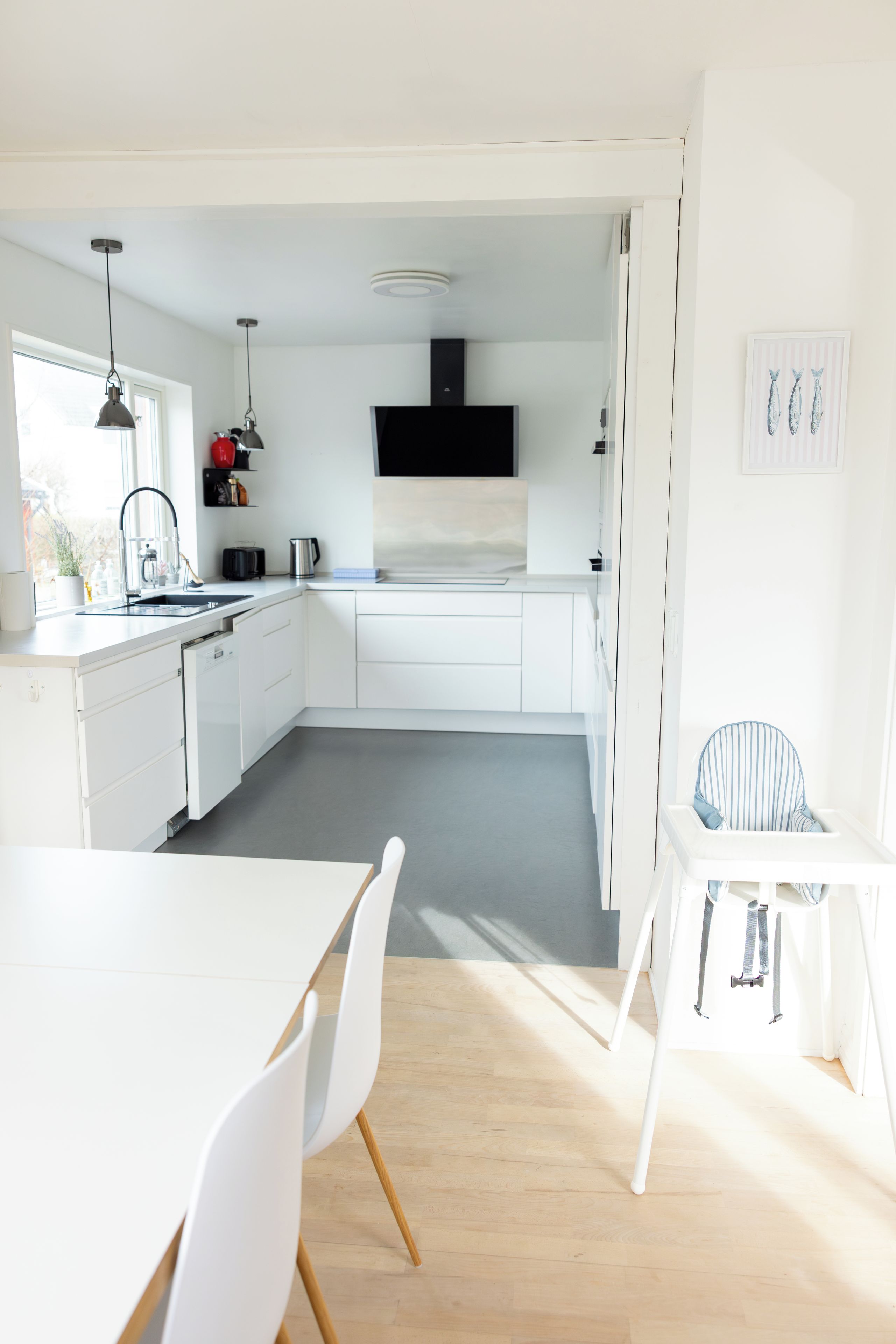 A modern kitchen with white cabinetry, a black range hood, and a dining area with a white table and chairs.