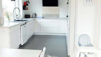 A modern kitchen with white cabinetry, a black range hood, and a dining area with a white table and chairs.