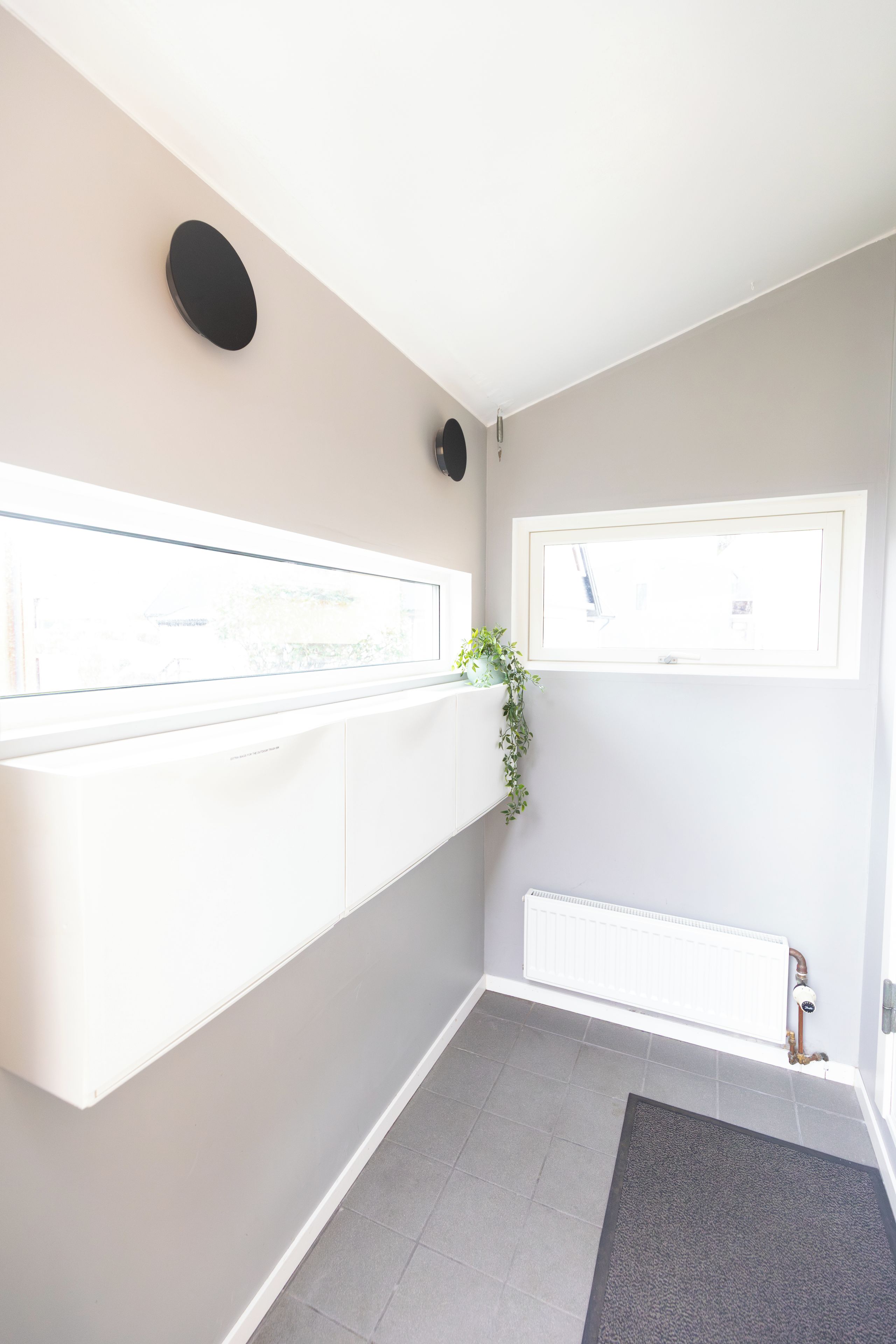 A modern bathroom with a white vanity, a radiator, a shower, and a small window.