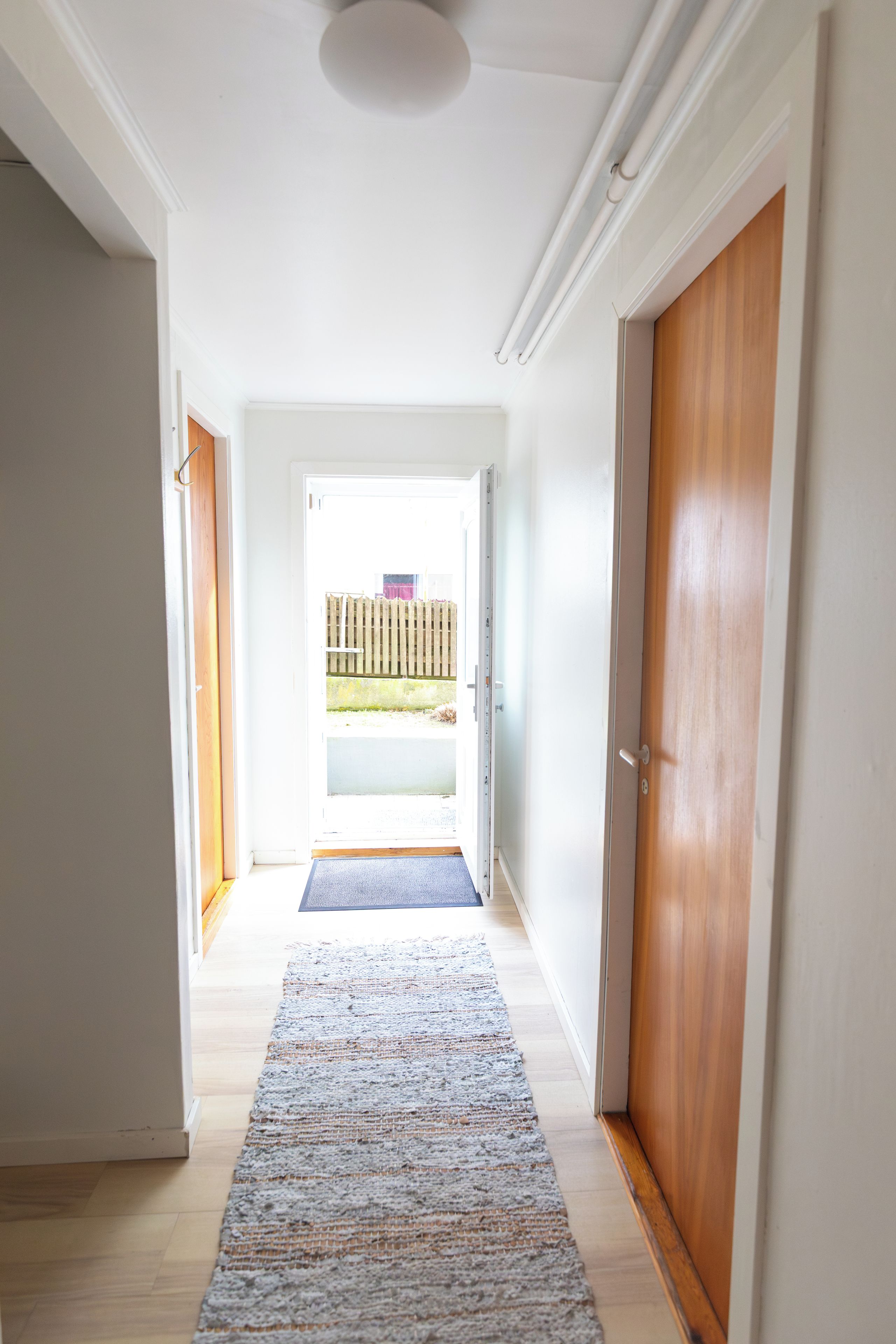 A hallway with a wooden door, a blue mat, and a view of the outside.