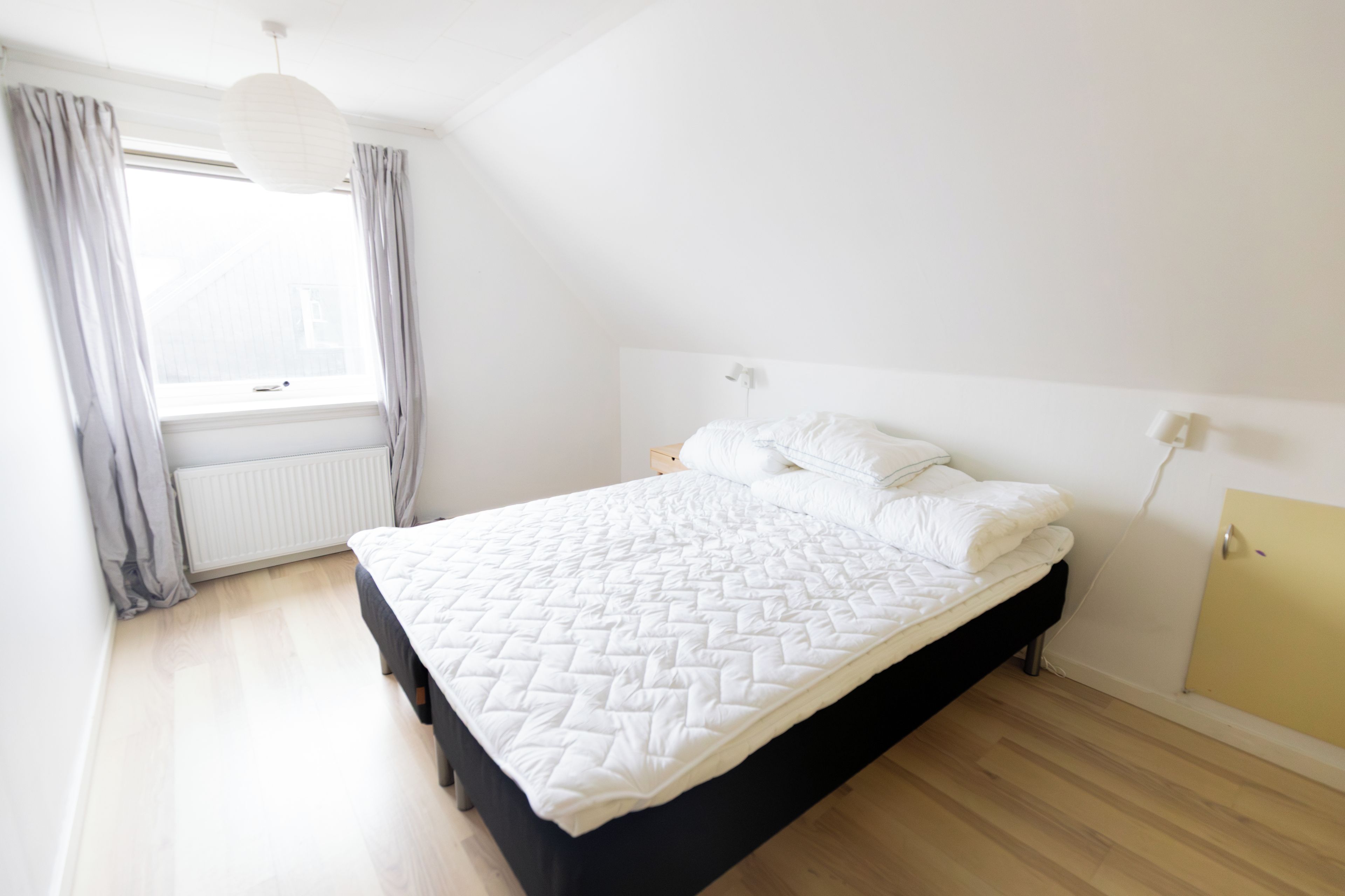 A bedroom with a bed, a window, a radiator, and a light fixture.