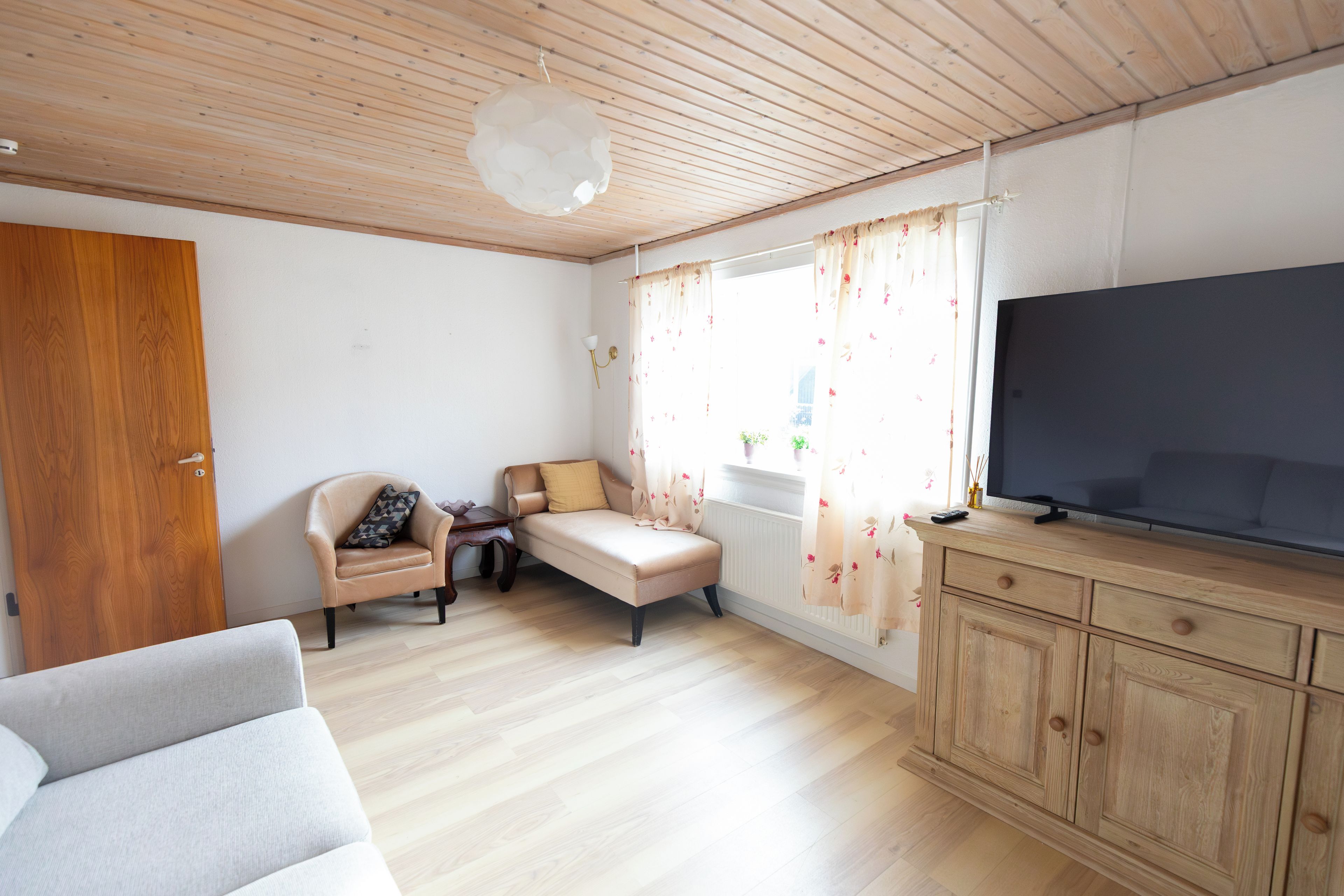 A room with a wooden ceiling, a sofa, a chair, a television, and a cabinet.