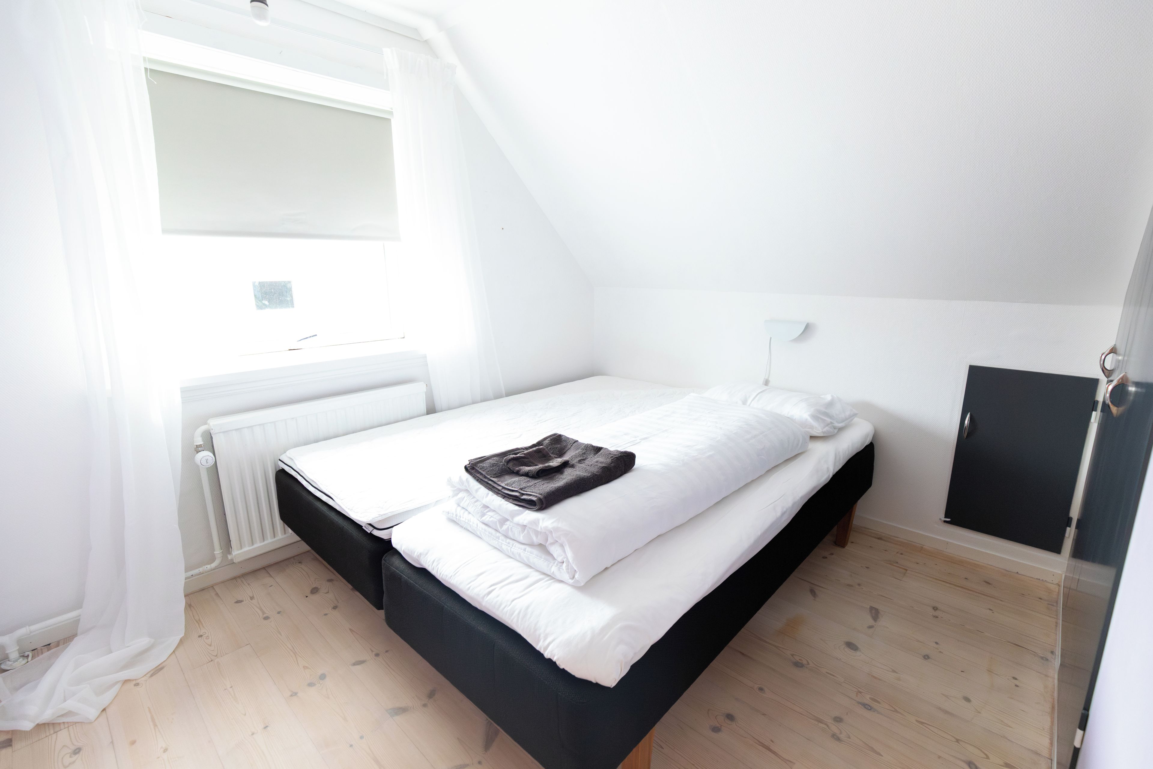 A single bed with white bedding, a black headboard, and a brown towel.