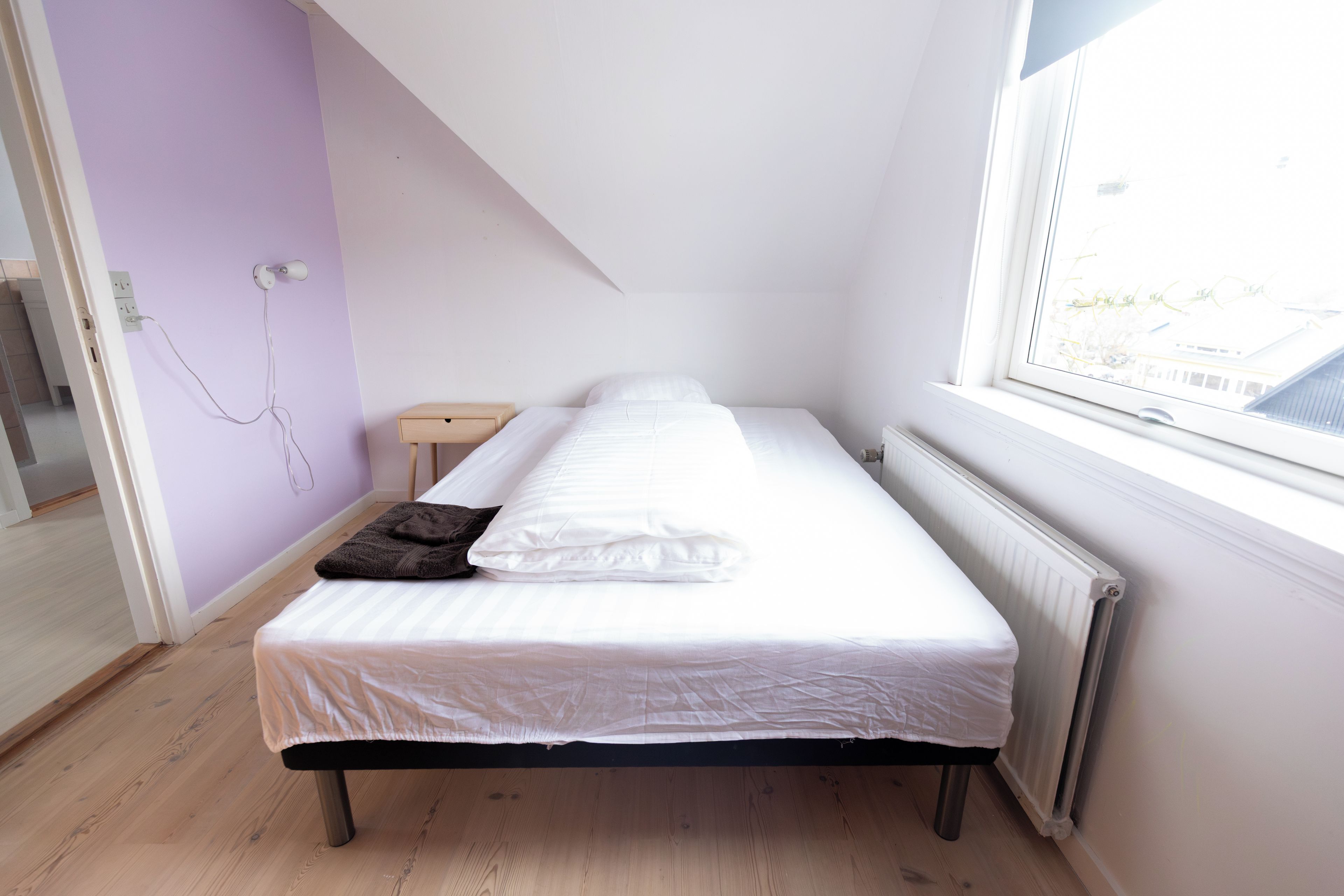 A single bed in a room with a sloped ceiling, a window, and a radiator.