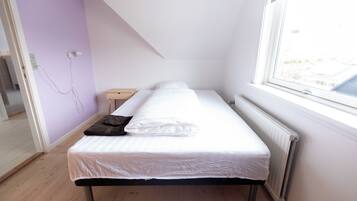 A single bed in a room with a sloped ceiling, a window, and a radiator.