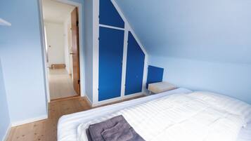 Un dormitorio con una cama, piso de madera, pared azul y una puerta que da a otra habitación.