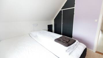 Een slaapkamer met een bed, een kledingkast en een schuine kap.