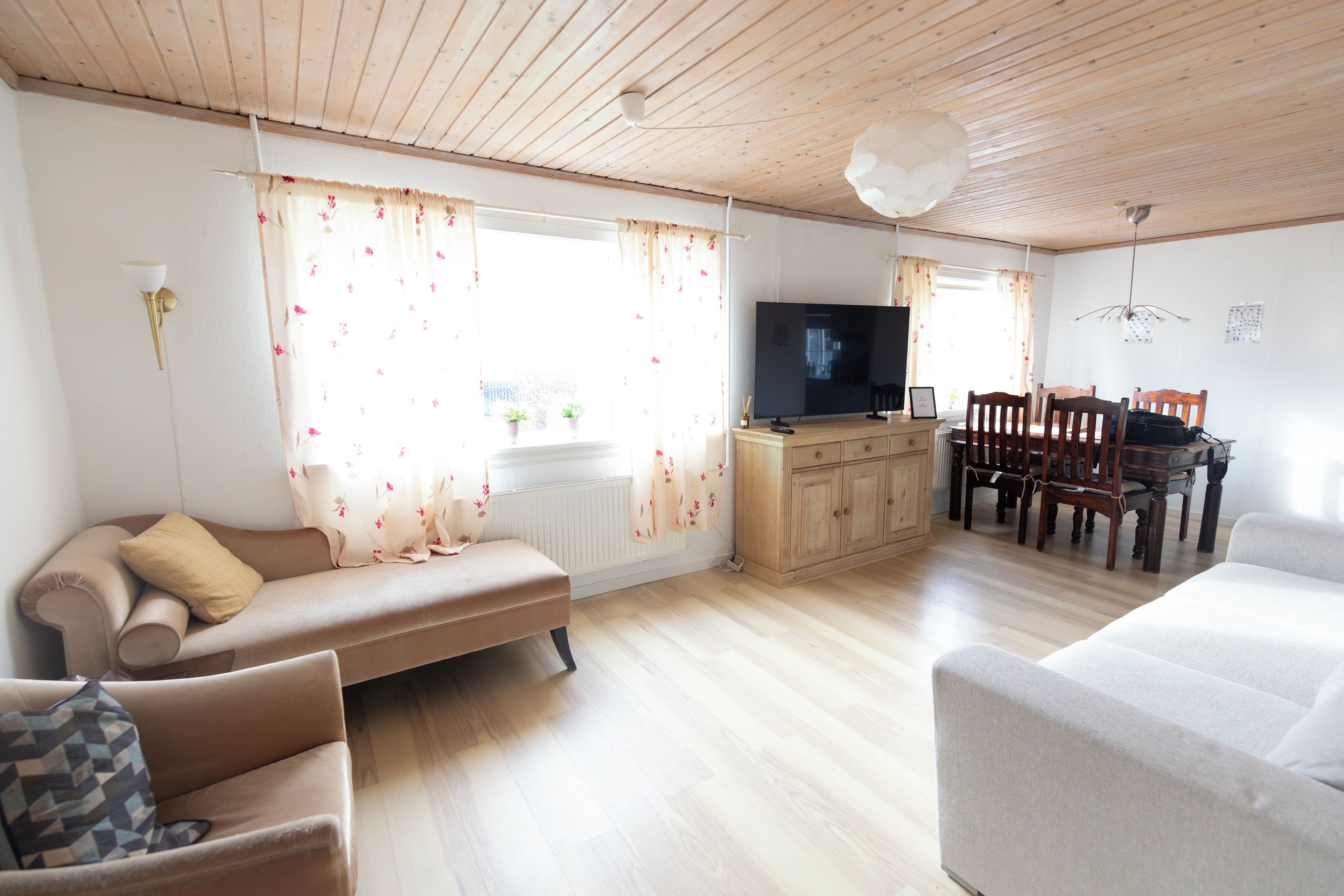 Una sala de estar con sofá, televisor, mesa de comedor y techo de madera.