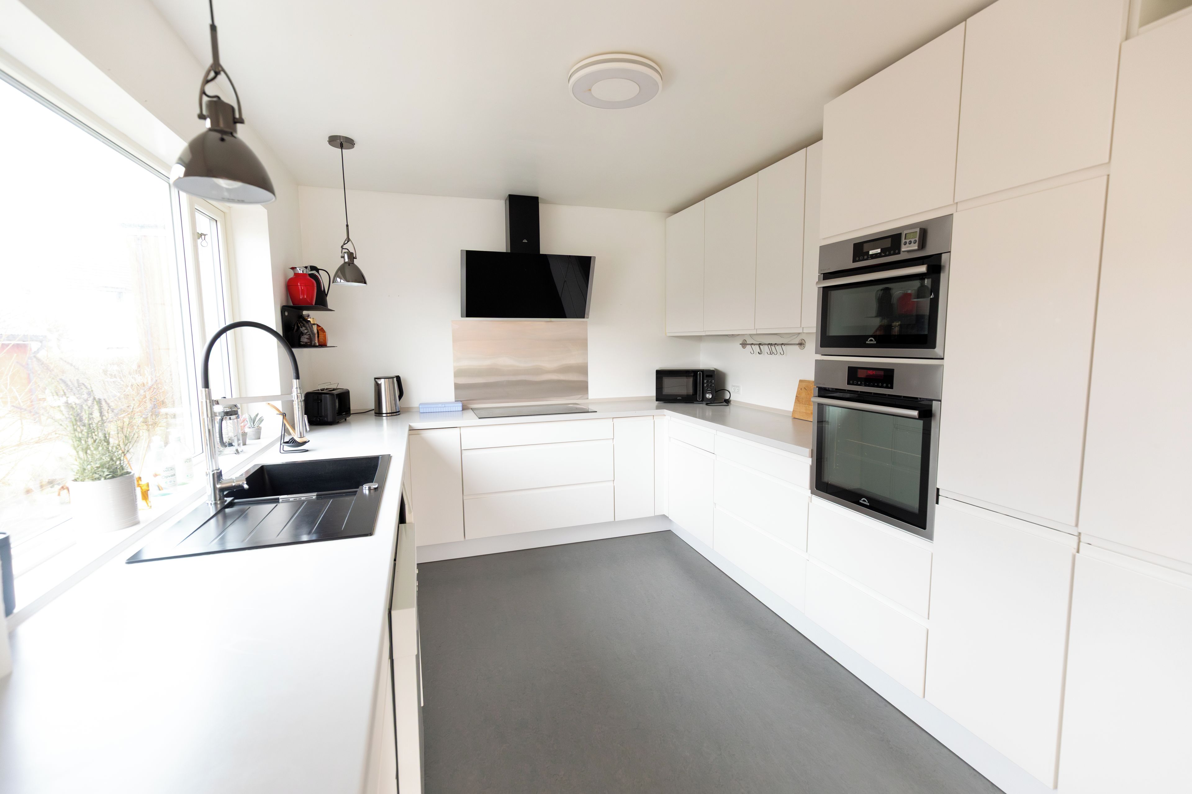 A modern kitchen with white cabinetry, a built-in oven, a microwave, and a stainless steel sink.