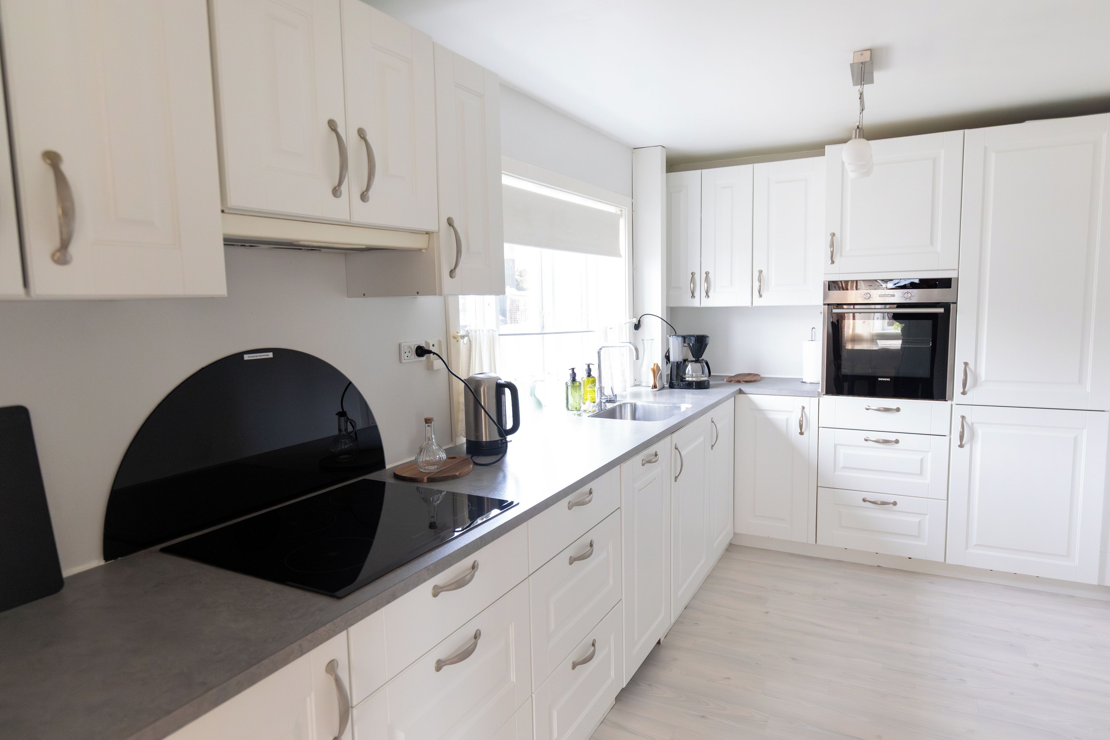 Una cocina moderna con armarios blancos, una placa de cocción por inducción negra y un horno empotrado.