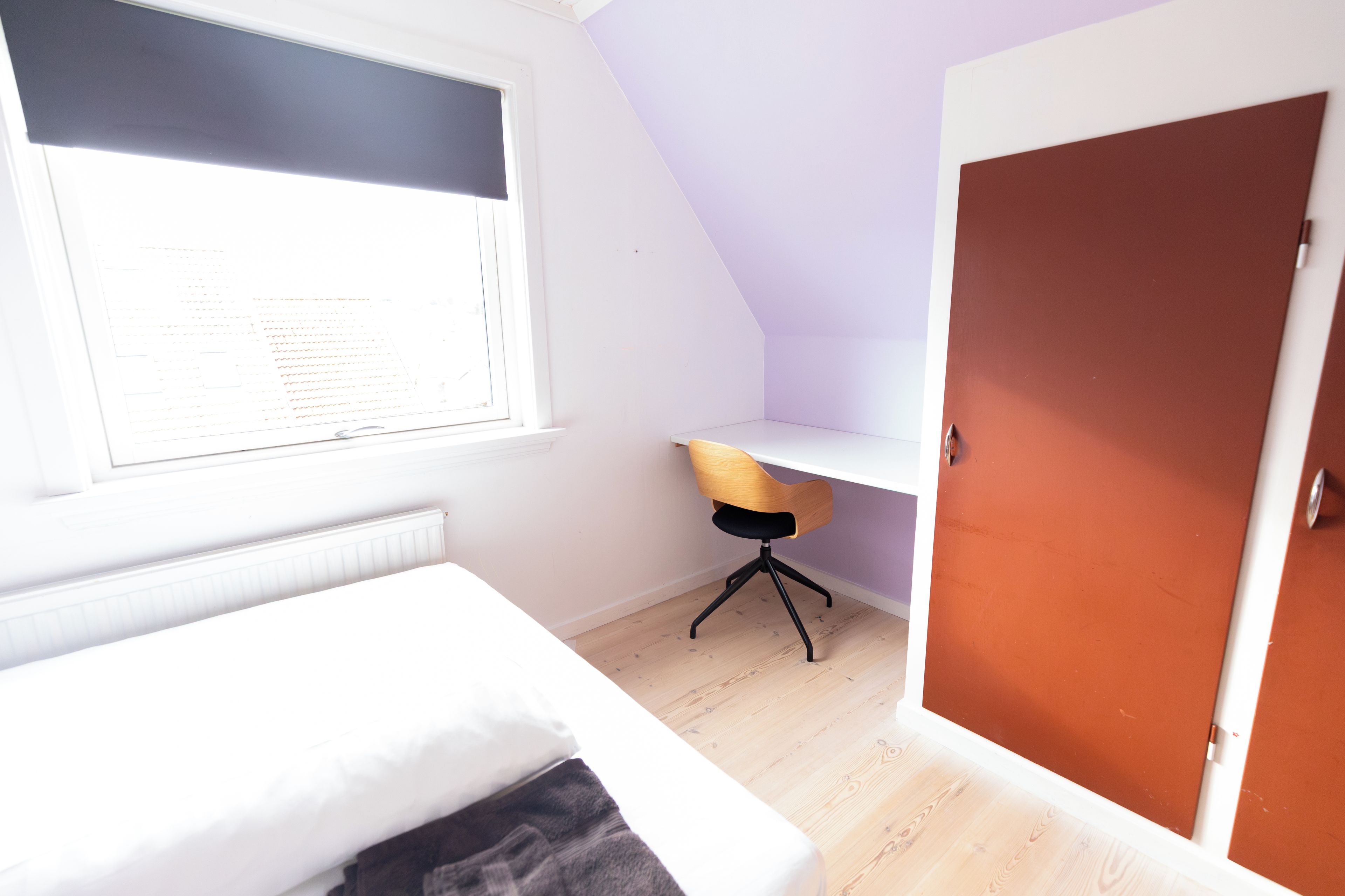 A bedroom with a bed, a desk, and a door.