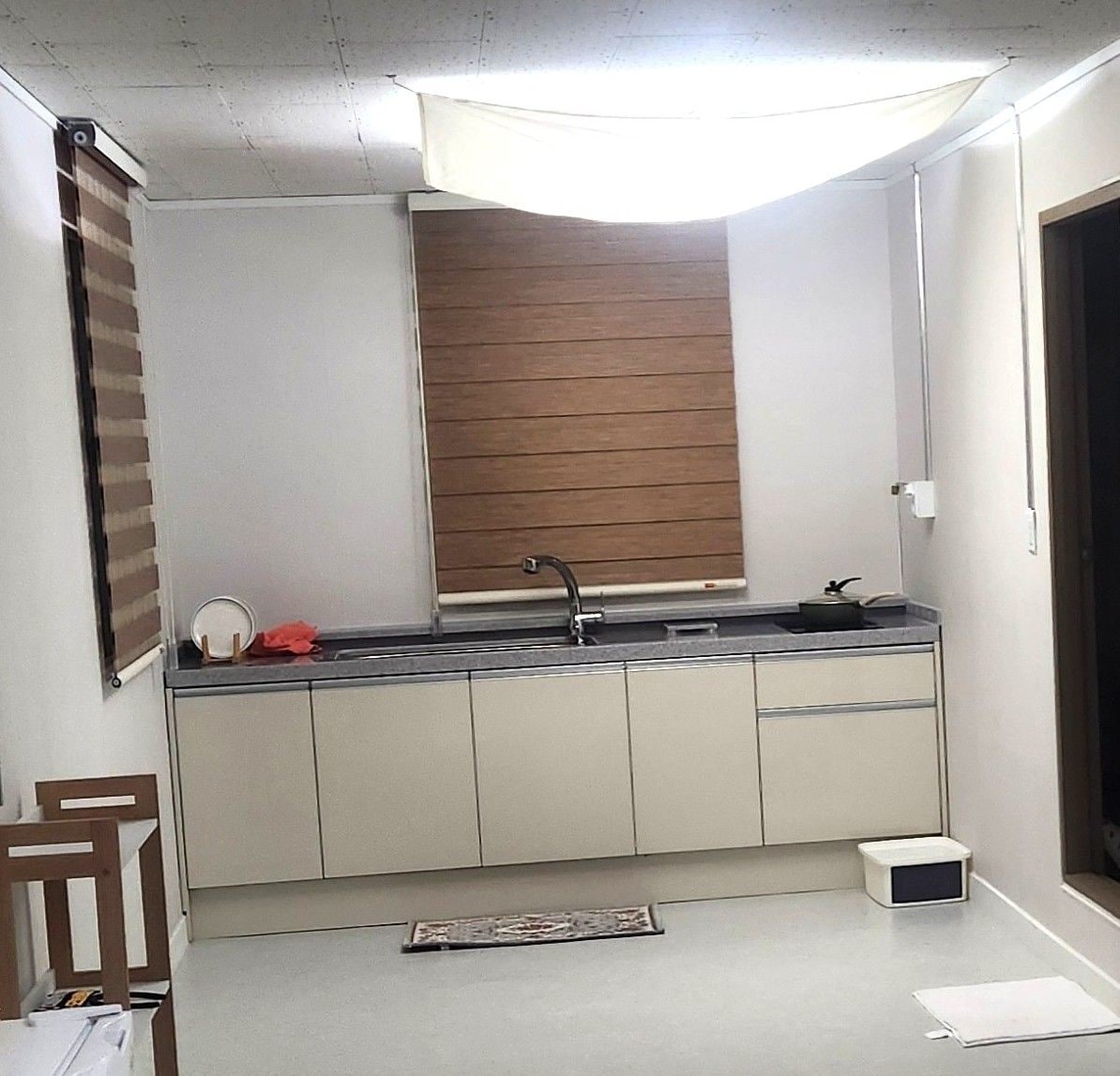 A compact kitchen with a built-in sink, a window with blinds, and a small trash bin.