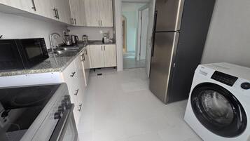 A modern kitchen with stainless steel appliances, light wood cabinets, and a built-in washing machine.