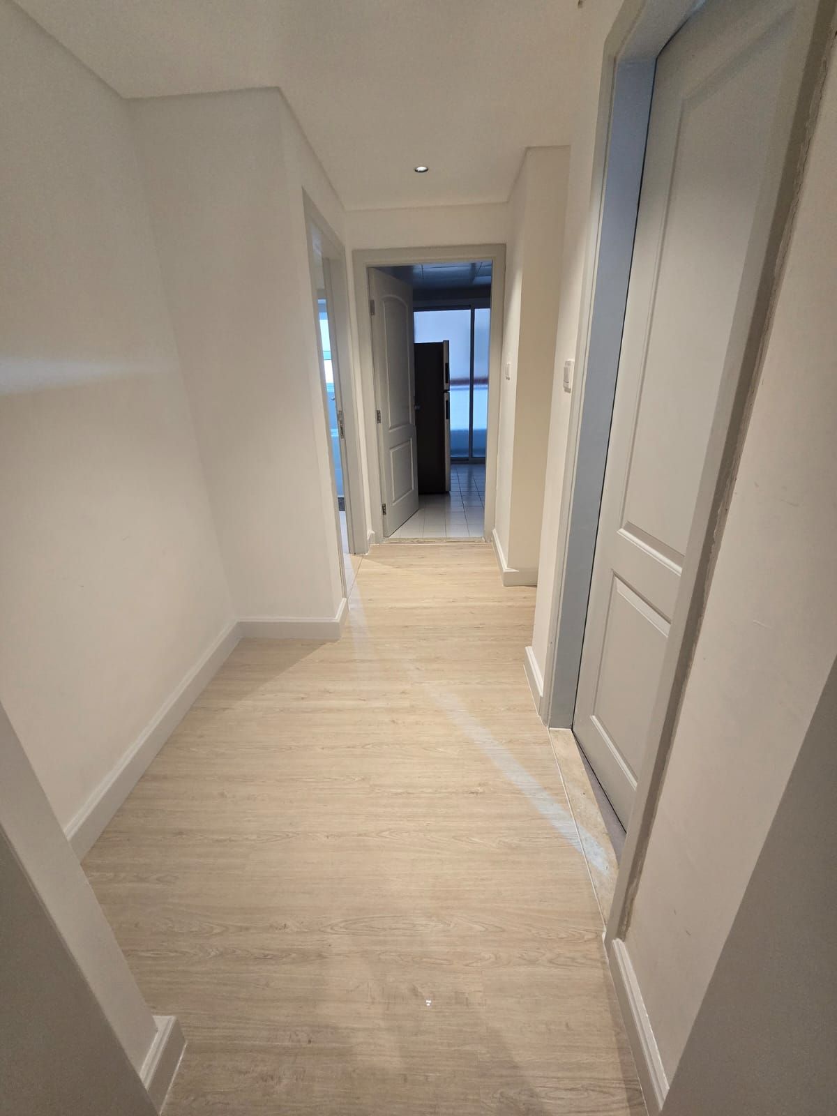 A hallway with a wooden floor and white walls, leading to a door at the end.