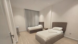 Una camera d'albergo moderna con due letti, un comodino, una lampada e un'ampia finestra con tende.